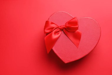 Sevgililer Günün kutlu olsun. Kırmızı arka planda kalp şeklinde hediye kutusu, üst manzara. Metin için boşluk