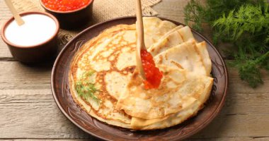 Ahşap masada lezzetli kreplere kırmızı havyar ekliyorum, yakın plan. Kamera içeri giriyor.