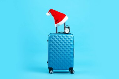 Noel tatili. Kırmızı Noel Baba şapkalı bavul ve açık mavi arka planda alarm saati.