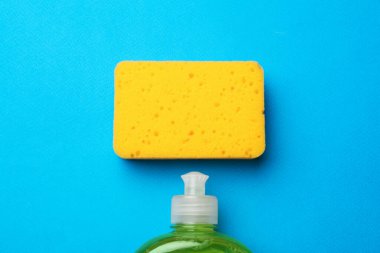 Açık mavi zemin üzerinde mutfak süngeri ve bulaşık sabunu, düz yatıyordu.