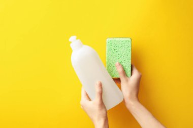 Turuncu arka planda sünger ve bulaşık deterjanı tutan kadın. Metin için boşluk