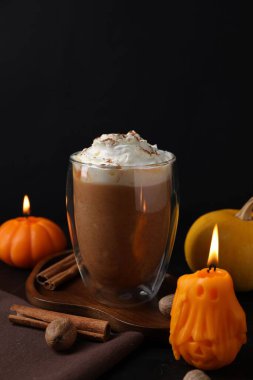 Krem şantili balkabaklı latte ve siyah arka planda sonbahar dekoru, yakın plan.