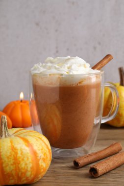 Cam bardakta kremalı balkabaklı latte, tarçın çubukları, taze sebzeler ve ahşap masada yanan mum gri arka planda, yakın planda.