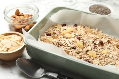 Tahıl yapıyorum. Yulaf gevreği, kurutulmuş meyve, badem fıstığı ve bal beyaz mermer masada, yakın plan.