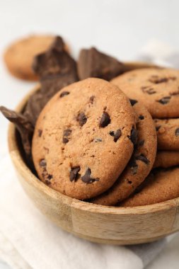 Lezzetli çikolatalı kurabiyeler ve beyaz masadaki çikolata parçaları, yakın plan.