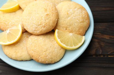 Lezzetli limonlu kurabiyeler ve siyah ahşap masada meyve dilimleri, yakın plan.