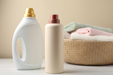 Çamaşır sepetinde havlular ve beyaz ahşap masadaki deterjan bej arka planda, yakın plan.