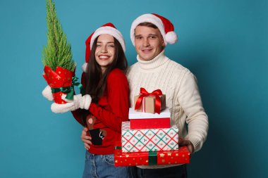 Noel Baba şapkalı mutlu bir çift ve açık mavi arka planda Noel hediyeleri.