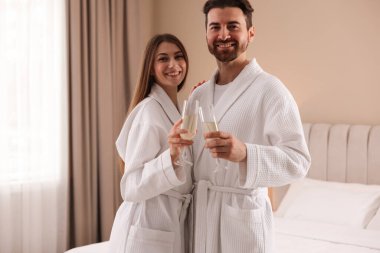 İçeride köpüklü şarap bardakları olan bornozlu mutlu çift.