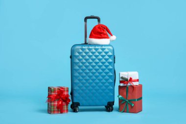 Noel tatili. Kırmızı bavul, Noel Baba şapkası ve açık mavi arka planda hediye kutuları.