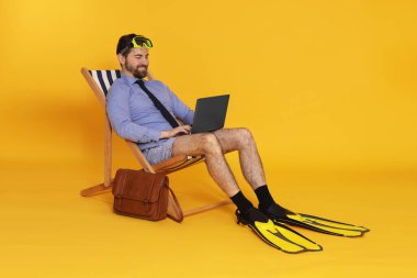 Dalış maskesi, dizüstü bilgisayarı ve turuncu arka planda yüzgeçli sandalyesi olan bir iş adamı.