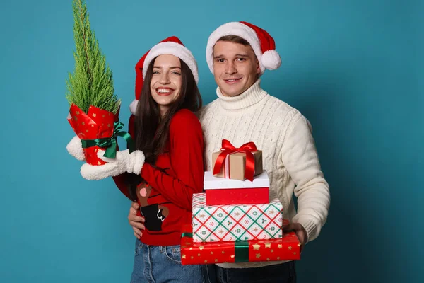 Noel Baba şapkalı mutlu bir çift ve açık mavi arka planda Noel hediyeleri.