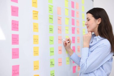Ofisinde yapışkan notlar olan beyaz tahtanın yanında elinde kalem tutan kadın.