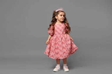 Saç bandı takmış şirin küçük bir kız ve gri arka planda giyiniyor.