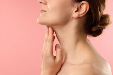 Pembe arka planda boynuna dokunan kadın, yakın plan. Metin için boşluk