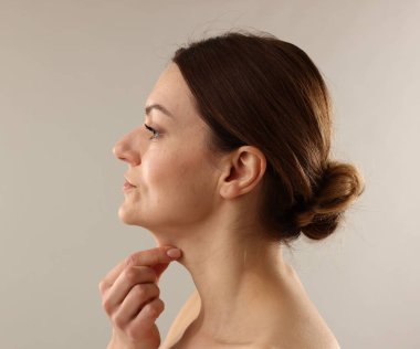 Açık gri arka planda boynuna dokunan kadın.