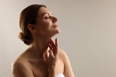 Açık gri arkaplanda boynuna dokunan kadın, metin için boşluk