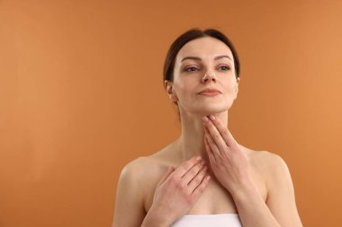 Soluk turuncu arka planda boynuna dokunan kadın, mesaj için boşluk