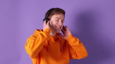 Kulaklıklı, müzik dinleyen ve menekşe arka planda dans eden bir adam.