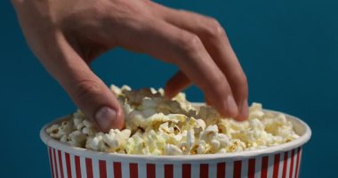 Açık mavi arka planda lezzetli patlamış mısır yiyen adam, yakın plan.