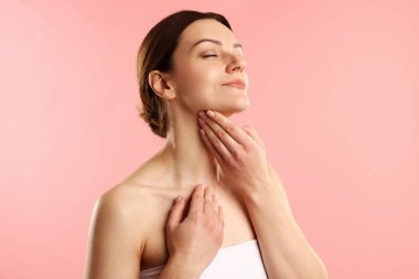 Kadın pembe arka planda boynuna dokunuyor.