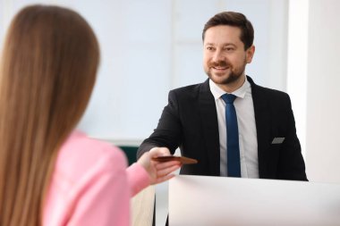 Resepsiyonist içeride misafir için pasaport veriyor.