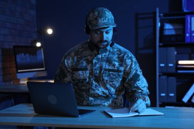Askerlik. Kulaklıklı bir asker, gece ofiste ahşap masada çalışıyor.
