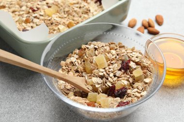 Tahıl yapıyorum. Yulaf gevreği, kurutulmuş meyve, badem fıstığı ve bal, gri desenli masa, yakın plan.