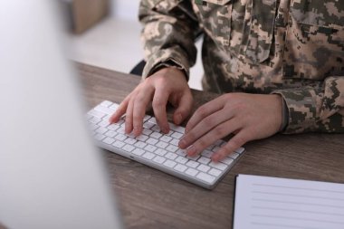 Askeri eğitim. Asker üniforması içindeki öğrenci ahşap masada öğreniyor, yakın plan.