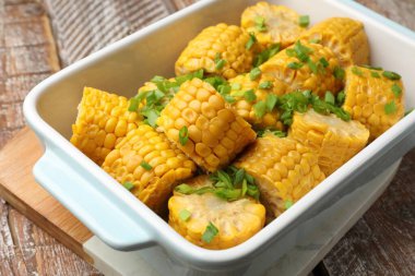 Haşlanmış mısır koçanı parçaları ve ahşap masada yeşil soğan, yakın plan.