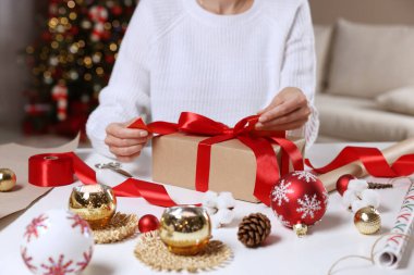 Beyaz masada Noel hediyesini paketleyen kadın, yakın plan.