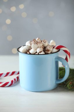 Şekerlemeli lezzetli kakao, baston şekerler ve beyaz ahşap masa üzerindeki Noel süsü bulanık ışıklara karşı, yakın çekim. Bokeh etkisi