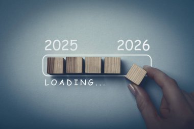 Yeni yıl 2026. Gri arka planda yükleme çubuğuna tahtadan küpü diğerlerinin yanına koyan kadın, üst görünüm