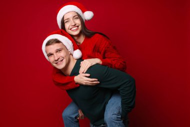 Noel Baba şapkalı gülümseyen çift kırmızı arka planda eğleniyor. Mutlu Noeller ve mutlu yıllar.