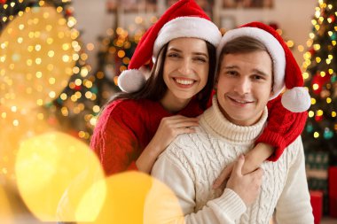 Noel Baba şapkalı, evde bulanık ışıklara karşı gülümseyen bir çift. Mutlu Noeller ve mutlu yıllar.