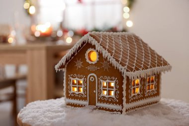 Güzel zencefilli kek evi ve masa üzerindeki yapay kar kapalı alanda bulanık ışıklara karşı, yakın çekim. Noel atmosferi