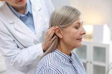 Doktor klinikte hastanın kulağına işitme cihazı takıyor.