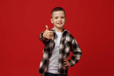 Kırmızı arka planda başparmak gösteren sevimli küçük çocuk.