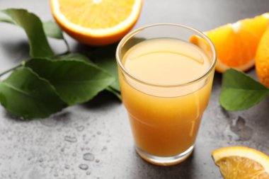 Taze portakal suyu, meyveler ve yapraklar gri masada, yakın plan.