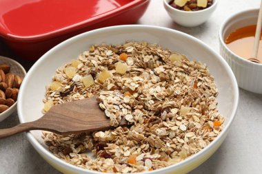 Tahıl yapıyorum. Bir kase yulaf ezmesi, bal ve kuru meyveler açık gri masada, yakın plan.