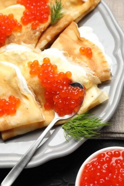 Kırmızı havyarlı leziz krepler ve siyah masada ekşi krema, yakın plan.