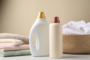 Çamaşır sepetini ve beyaz ahşap masada deterjan şişelerini bej arka planda, yakın plan.