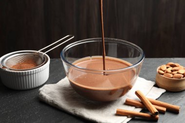 Sıvı çikolata hamuru siyah masada cam kaseye akıyor, yakın plan.