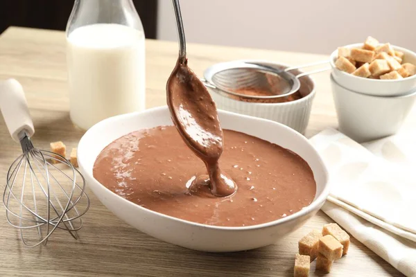 Sıvı çikolata hamuru ahşap masada kaseye akıyor.
