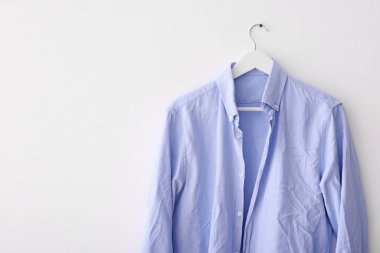 Beyaz duvarda asılı açık mavi buruşuk gömlek. Metin için boşluk