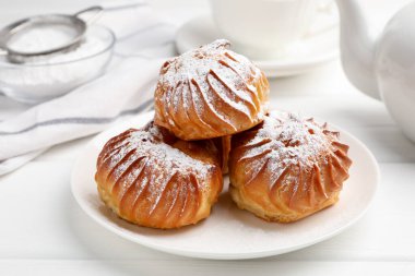 Beyaz ahşap masada servis edilen pudra şekerli lezzetli profiteroller.