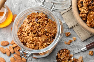 Cam kavanozda lezzetli granola ve açık gri masada malzemeler, düz uzanmış.