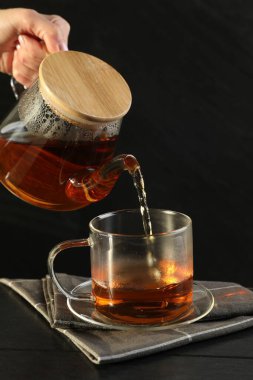 Siyah ahşap masada çaydanlıktan fincana sıcak çay dolduran kadın, yakın plan.