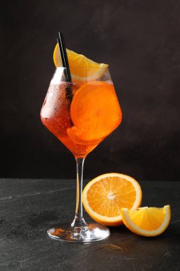 Bir bardak ferahlatıcı spritzer kokteyli ve siyah masada portakal dilimleri.