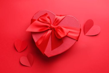 Sevgililer Günün kutlu olsun. Kalp şeklinde hediye kutusu ve kırmızı arka planda kağıt kalpler, düz yatıyordu.